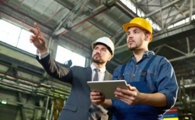 Waist up portrait of handsome businessman pointing up while discussing something with factory worker holding digital tablet, copy space