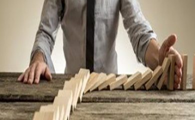 Businessman hand stopping domino effect. Rough wooden table with copy space.